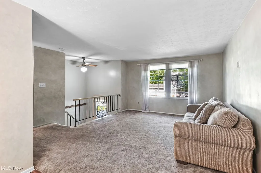 Living area featuring carpet, an upstairs landing, ceiling fan, and a textured ceiling