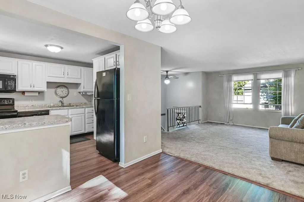 Kitchen with white cabinets, black appliances, open floor plan, dark wood-style flooring, and decorative light fixtures