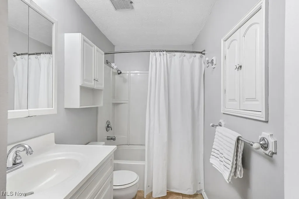 Full bath with vanity, shower / tub combo, a textured ceiling, and light tile patterned floors