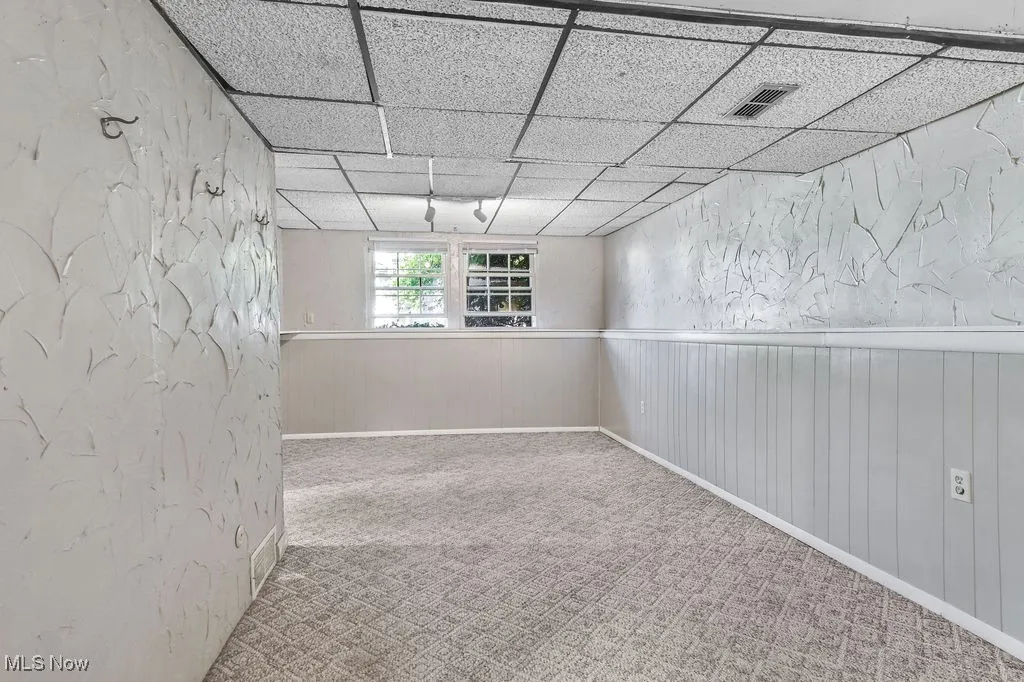 Carpeted family room with a paneled ceiling and wainscoting