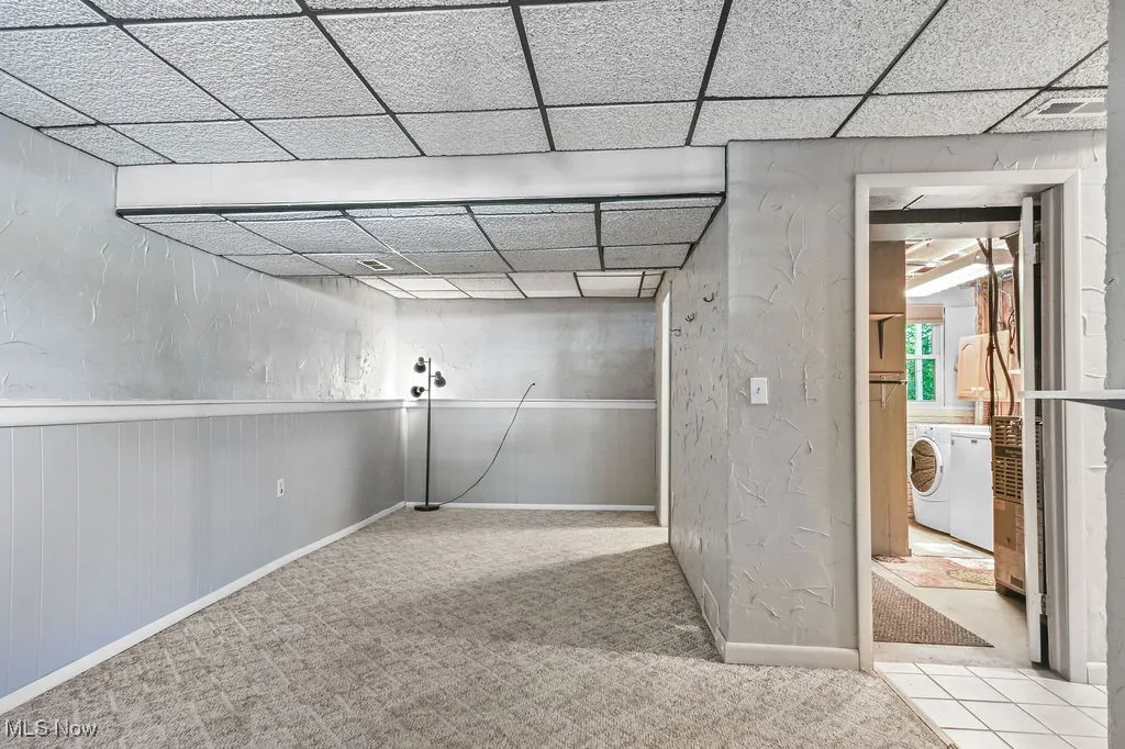 Family room with a paneled ceiling, a textured wall, light colored carpet, and a wainscoted wall. View into laundry/utility room.