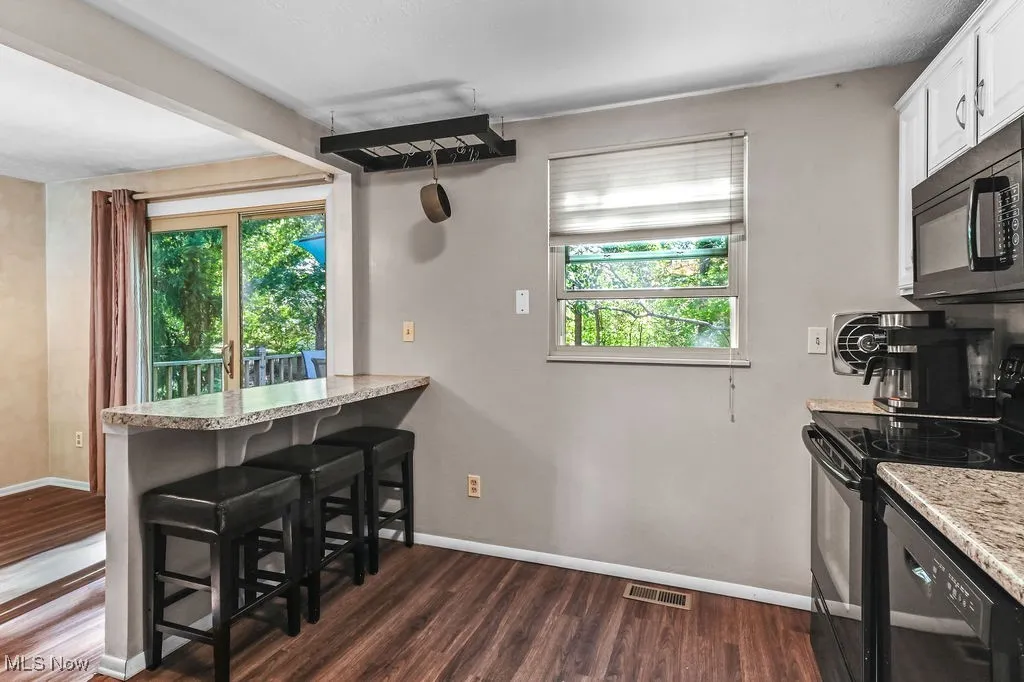 Kitchen featuring a kitchen breakfast bar, black appliances, light countertops, dark wood finished floors, and a peninsula