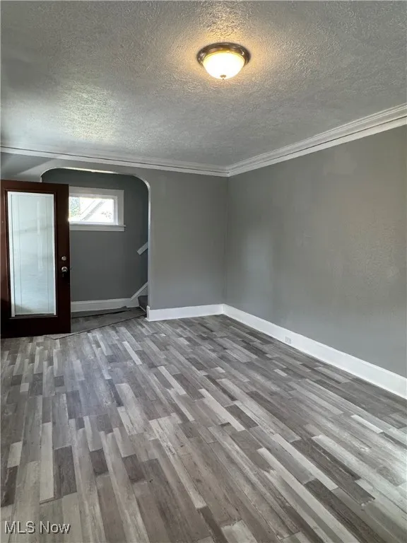 Spare room with arched walkways, wood finished floors, a textured ceiling, and crown molding