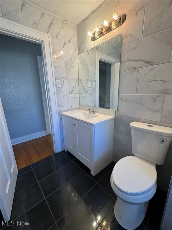 Half bath featuring tile walls, vanity, dark tile patterned flooring, and a textured ceiling