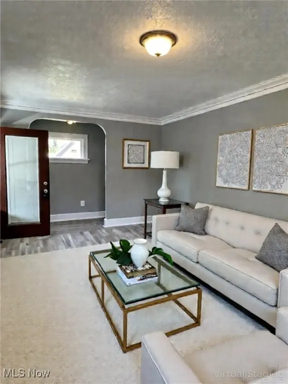 Living room featuring arched walkways, crown molding, a textured ceiling, and wood finished floors