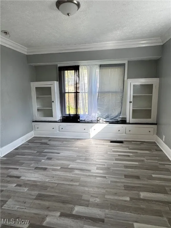 Unfurnished living room featuring a textured ceiling, crown molding, and wood finished floors