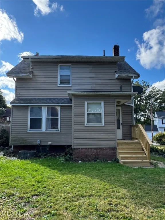 Back of house featuring a chimney, a yard, and a shingled roof