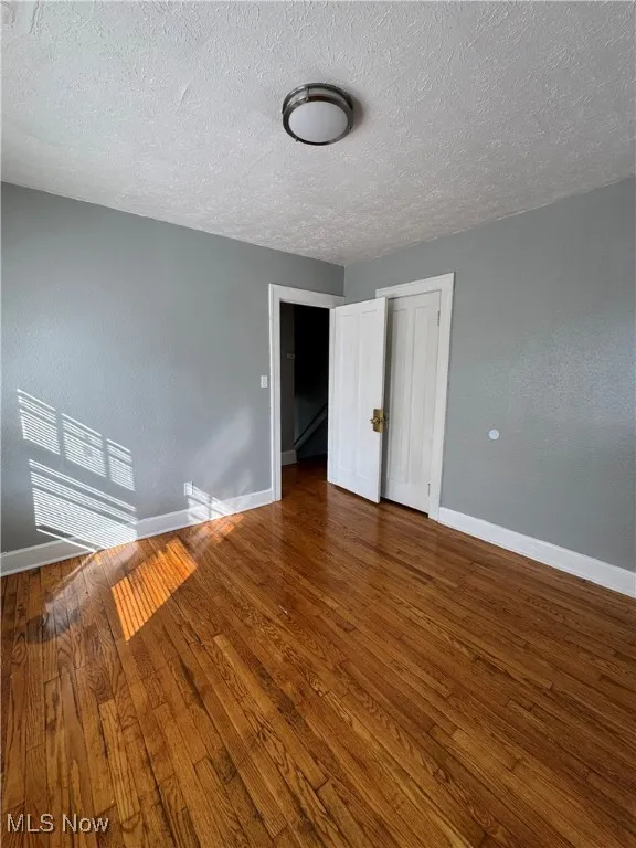 Unfurnished bedroom featuring hardwood / wood-style floors, a textured ceiling, a textured wall, and a closet