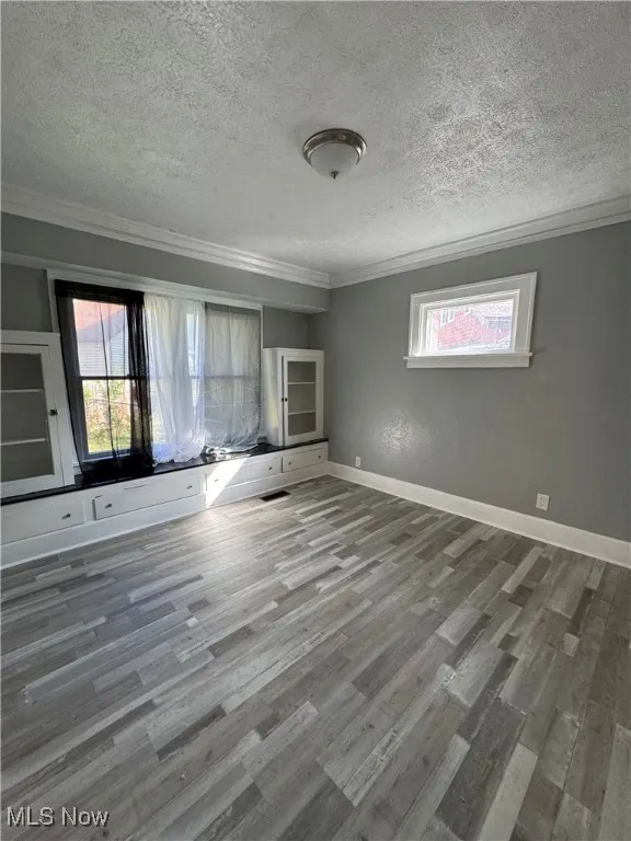 Unfurnished living room featuring plenty of natural light, wood finished floors, a textured ceiling, and ornamental molding