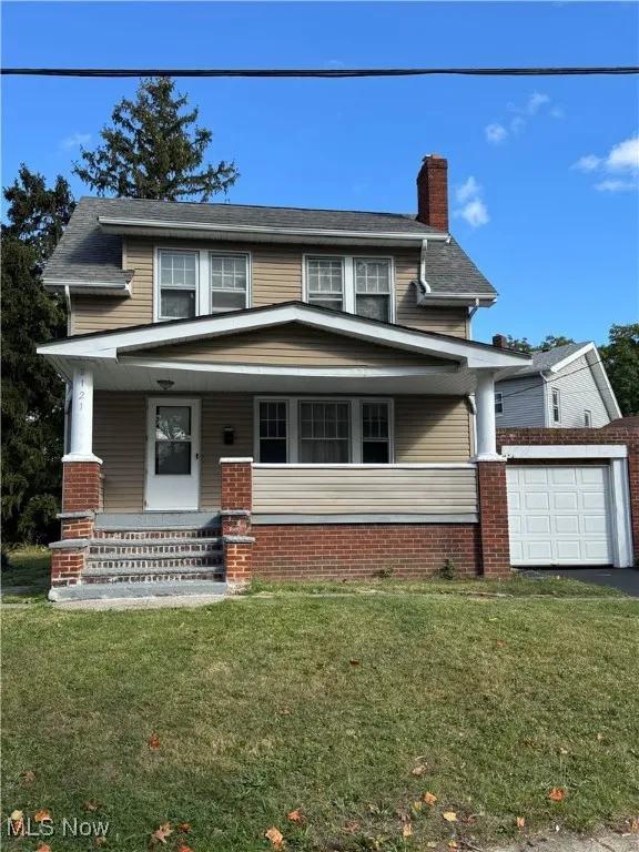 View of front of property featuring a chimney, covered porch, a garage, a front yard, and brick siding