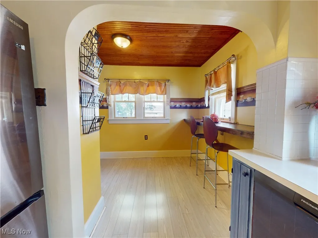 Kitchen with freestanding refrigerator, wooden ceiling, LVP flooring, arched walkways, and light countertops