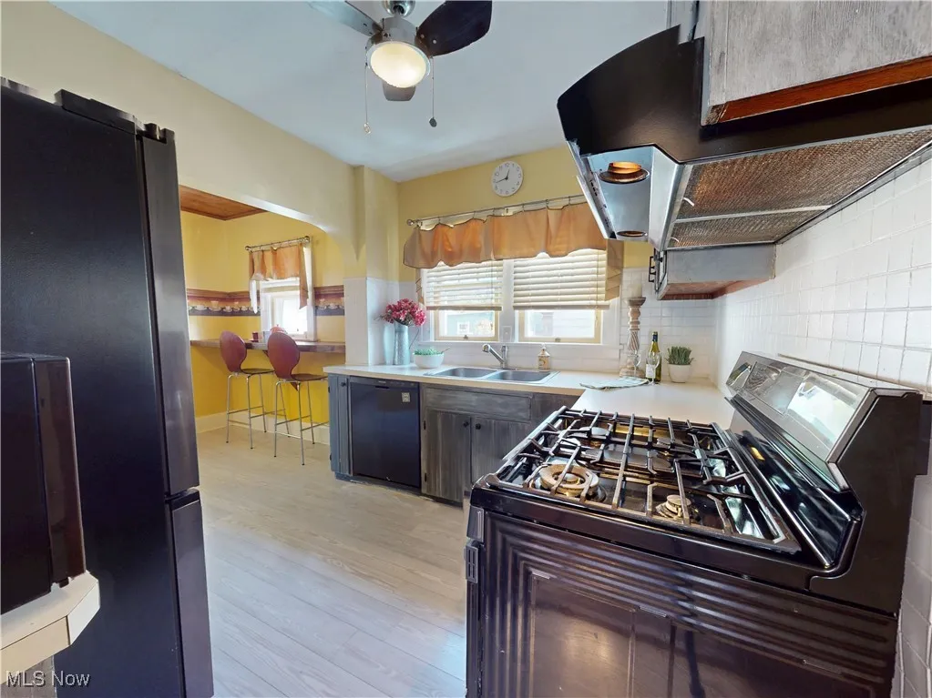 Kitchen featuring range hood, black appliances, backsplash, light wood-style flooring, and ceiling fan