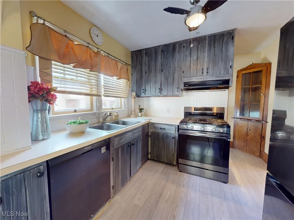 Kitchen with black appliances, light countertops, backsplash, light wood-style flooring, and range hood