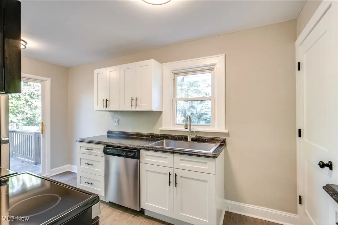 Kitchen featuring dark countertops, dishwasher, white cabinets, light wood-style flooring, and black / electric stove