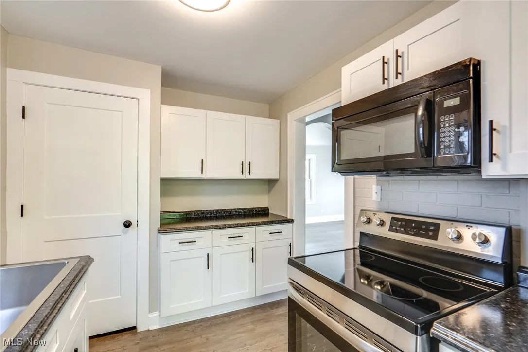Kitchen with electric stove, black microwave, white cabinetry, dark countertops, and light wood-style floors