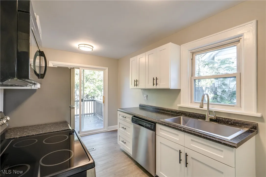 Kitchen with dark countertops, electric range, black microwave, stainless steel dishwasher, and light wood finished floors