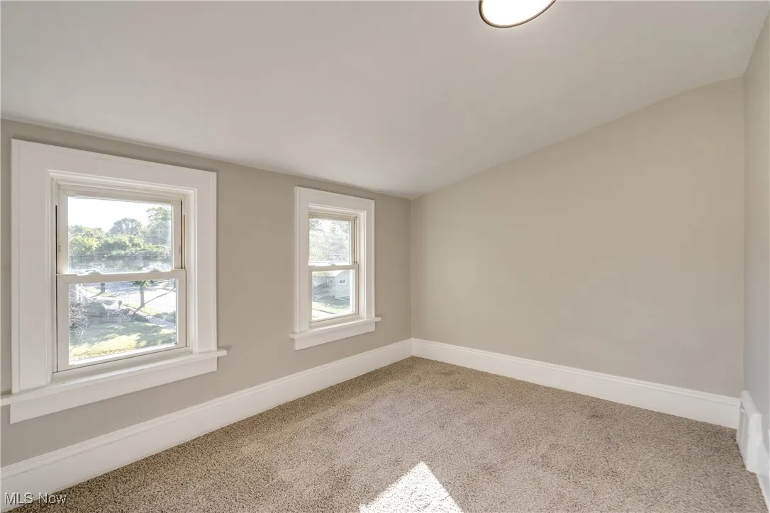 Carpeted spare room featuring baseboards and lofted ceiling