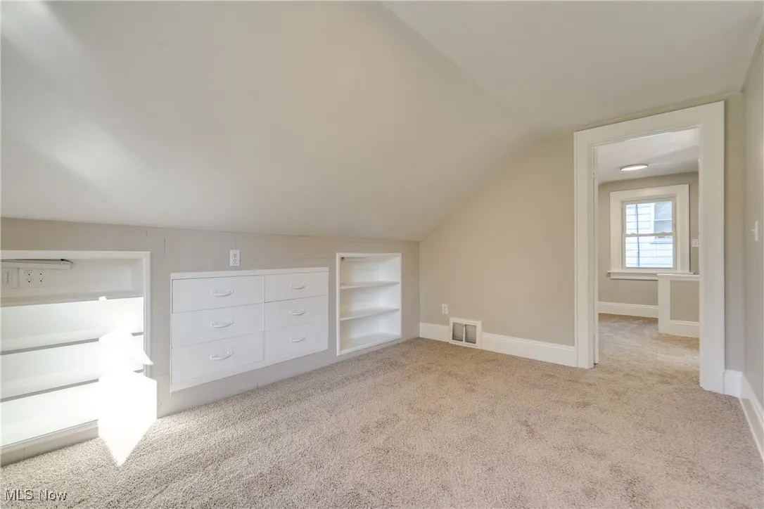 Additional living space with light colored carpet, built in shelves, and vaulted ceiling