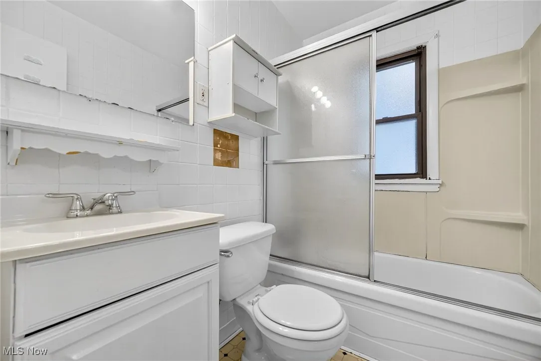 Full bathroom with enclosed tub / shower combo, tile walls, vanity, and decorative backsplash