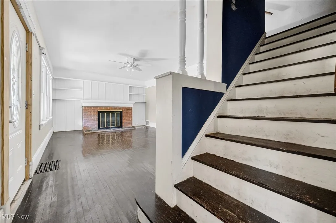 Stairs with hardwood / wood-style flooring, ceiling fan, and a fireplace