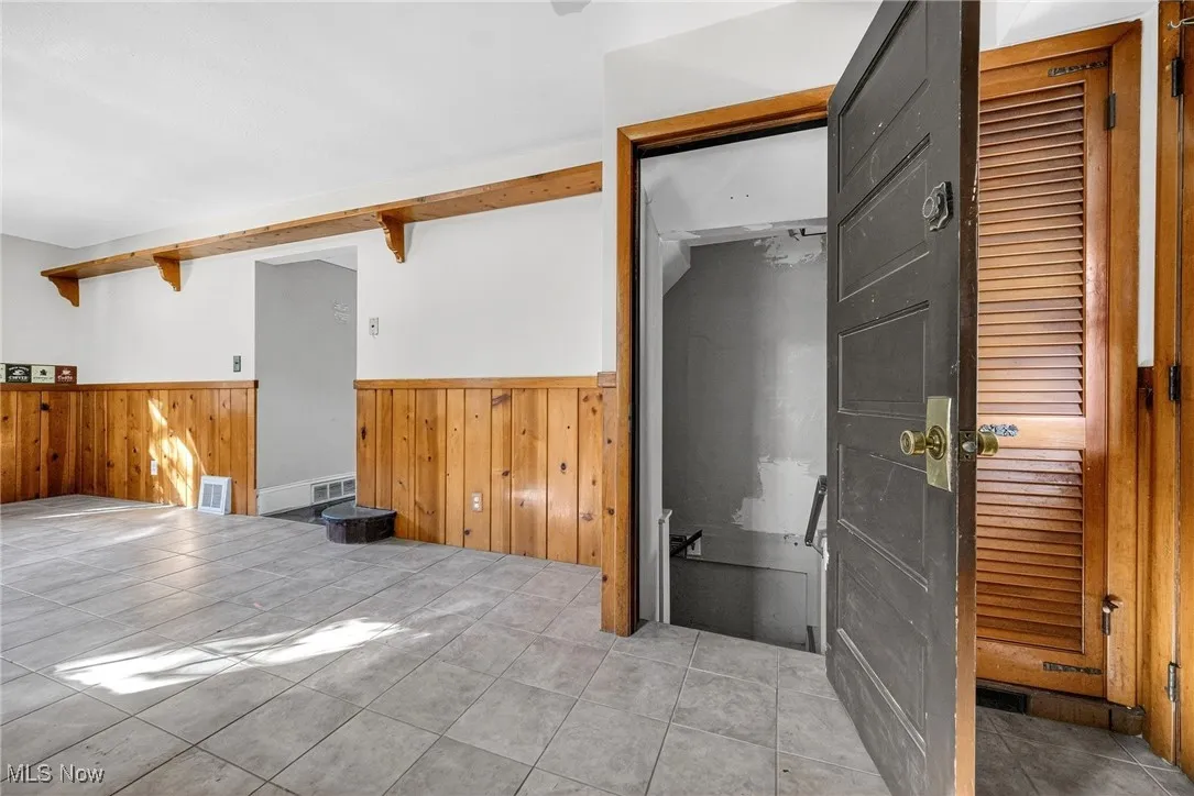 Empty room with wainscoting, tile patterned flooring, wood walls, and beamed ceiling