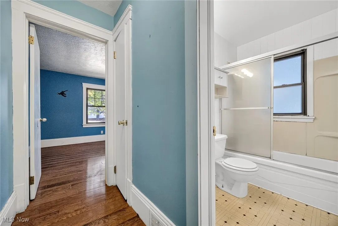 Bathroom featuring combined bath / shower with glass door and dark wood-type flooring