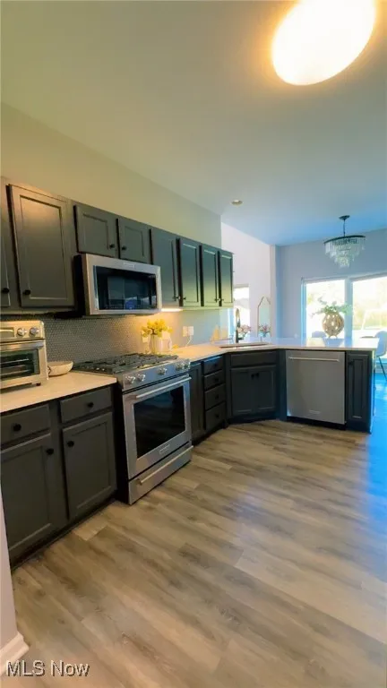 Kitchen with appliances with stainless steel finishes, light wood finished floors, decorative light fixtures, a chandelier, and gray cabinetry