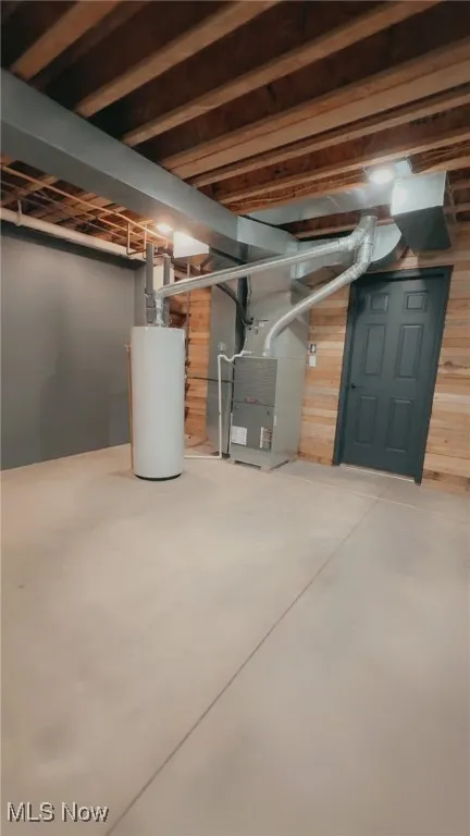 Unfinished below grade area featuring water heater, heating unit, and wooden walls