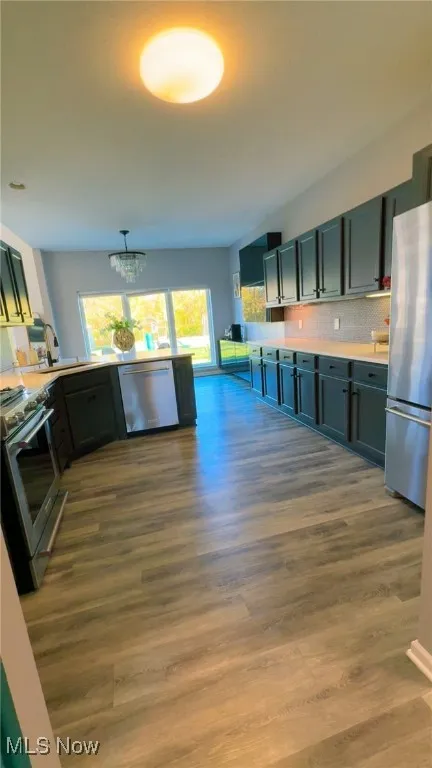 Kitchen with appliances with stainless steel finishes, dark wood finished floors, backsplash, and pendant lighting