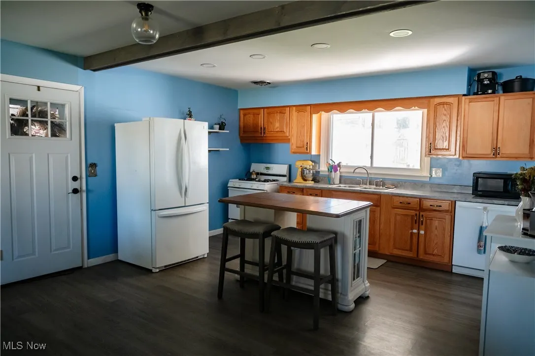 Kitchen featuring white appliances, a kitchen breakfast bar, brown cabinetry, dark wood finished floors, and beamed ceiling