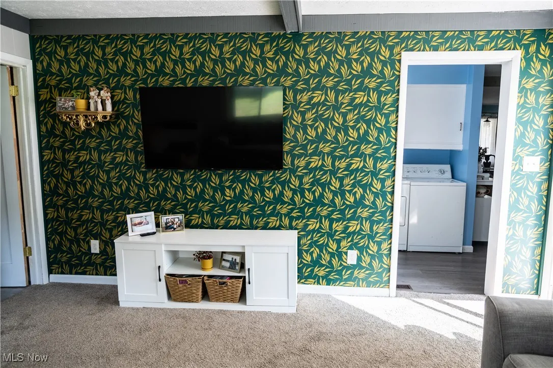 Unfurnished living room with wallpapered walls, washer / dryer, and carpet flooring