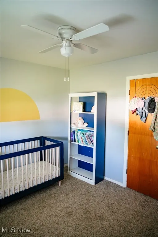 Bedroom featuring carpet flooring, a ceiling fan, and a crib