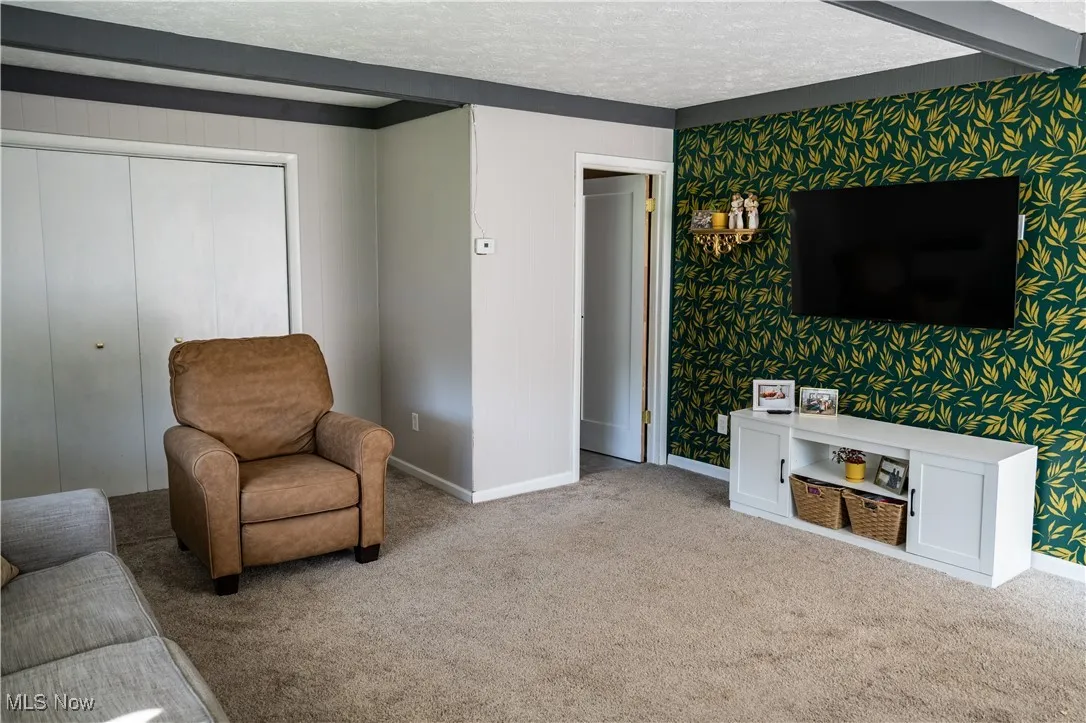 Living area featuring carpet, a textured ceiling, and wallpapered walls