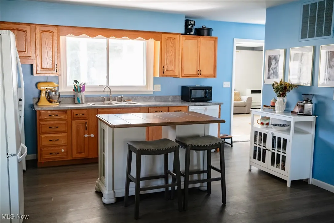 Kitchen featuring a breakfast bar area, tile countertops, white appliances, dark wood finished floors, and a center island