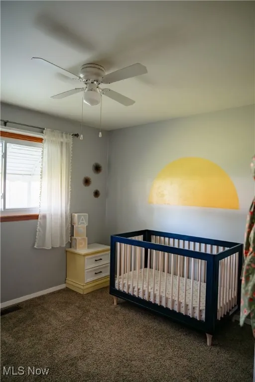 Bedroom featuring a crib, dark colored carpet, and a ceiling fan
