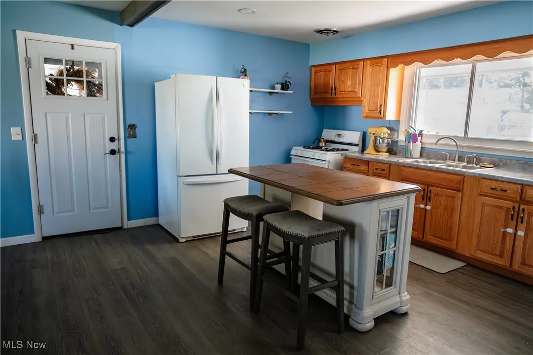 Kitchen featuring white appliances, a breakfast bar, brown cabinets, dark wood-style floors, and a center island