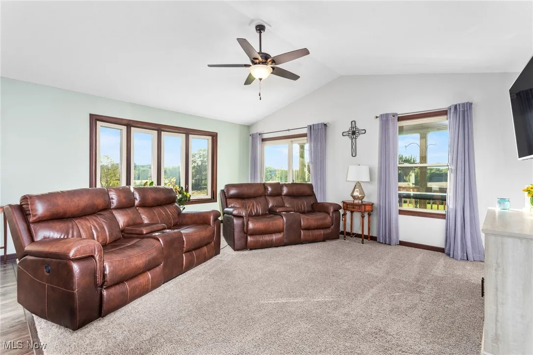 Carpeted living room with plenty of natural light, vaulted ceiling, and a ceiling fan