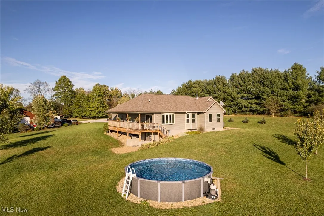 Rear view of property with a wooden deck, a yard, an outdoor pool, and stairs
