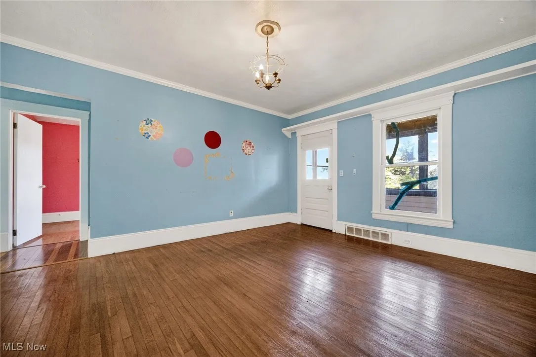 Unfurnished room with dark wood-style floors, crown molding, and a chandelier