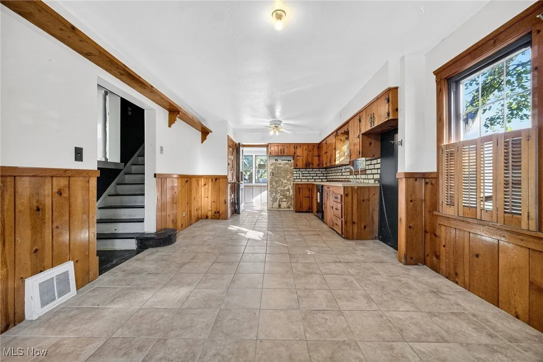 Kitchen with brown cabinetry, a wainscoted wall, wooden walls, light tile patterned floors, and light countertops