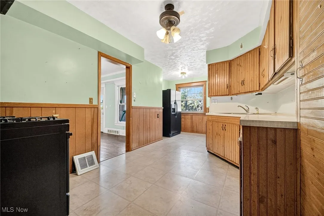 Kitchen with a wainscoted wall, light countertops, wooden walls, black refrigerator with ice dispenser, and brown cabinetry