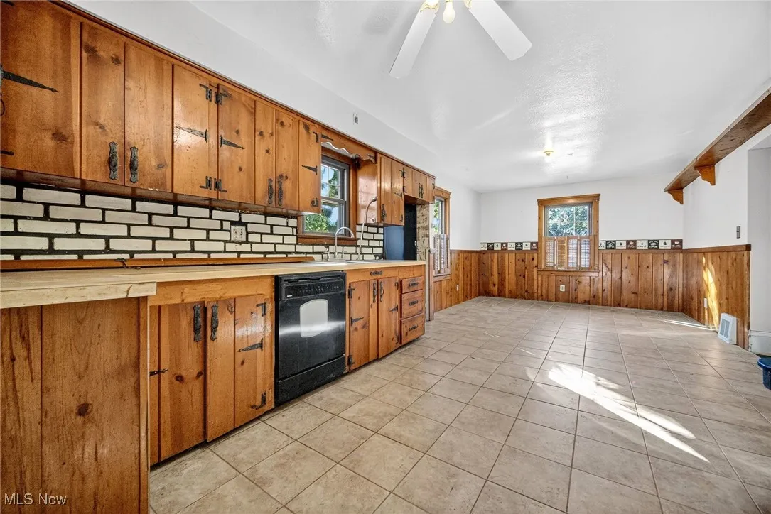Kitchen with brown cabinets, light tile patterned floors, dishwasher, wainscoting, and light countertops