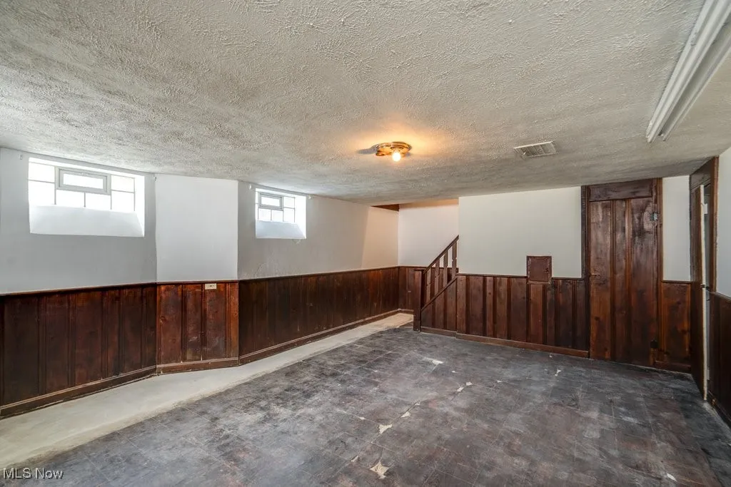 Below grade area featuring a wainscoted wall, wood walls, and a textured ceiling
