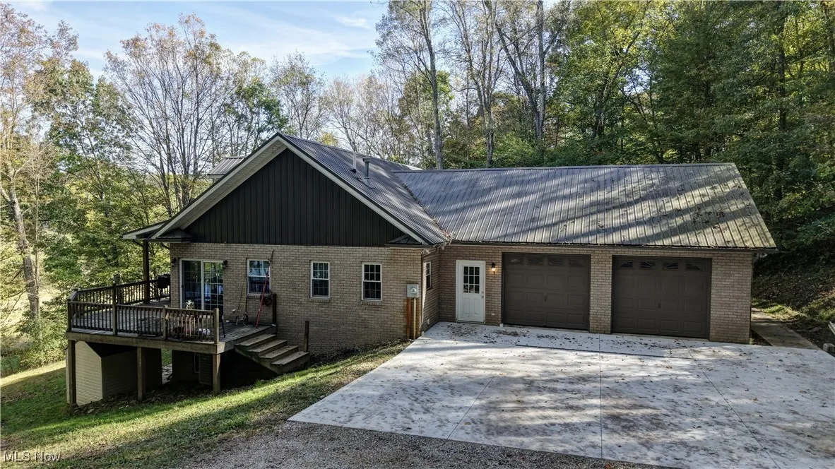 View of front of house featuring driveway, a wooden deck, a metal roof, and brick siding