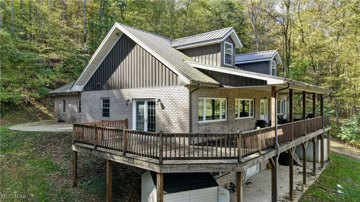 Back of property featuring a patio area, brick siding, a deck, board and batten siding, and a view of trees