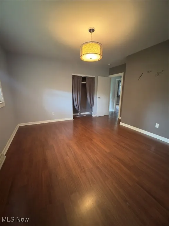 Unfurnished room featuring baseboards and dark wood-style flooring