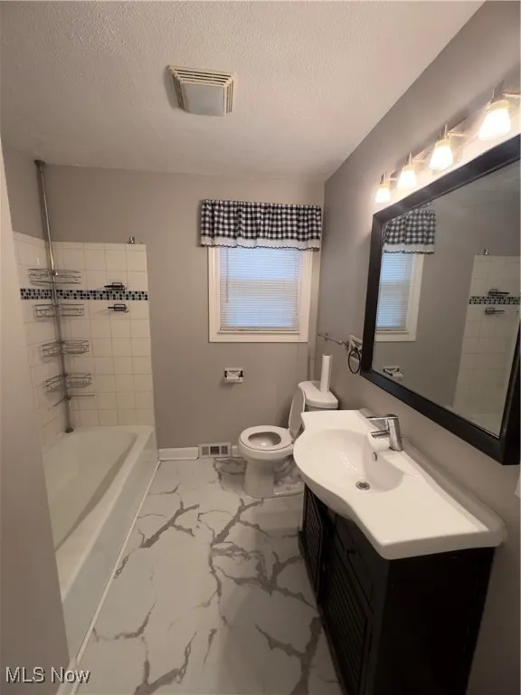 Full bath featuring a textured ceiling, vanity, washtub / shower combination, and light marble finish flooring