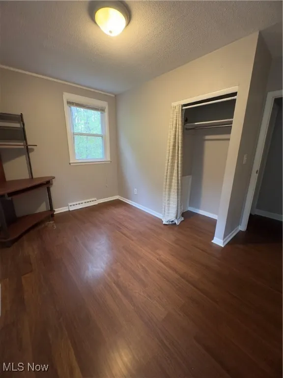 Unfurnished bedroom with a textured ceiling, dark wood-style floors, and a closet