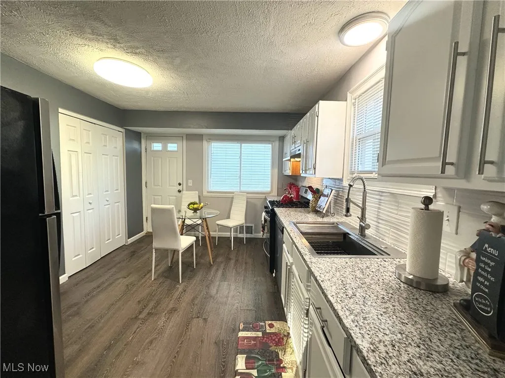 Kitchen featuring a textured ceiling, freestanding refrigerator, dark wood-style flooring, range with gas cooktop, and white cabinets