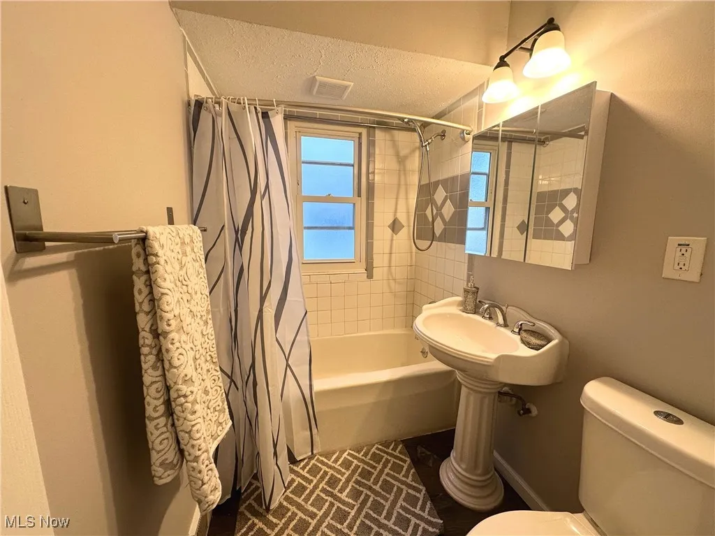 Full bath featuring shower / bath combination with curtain and a textured ceiling